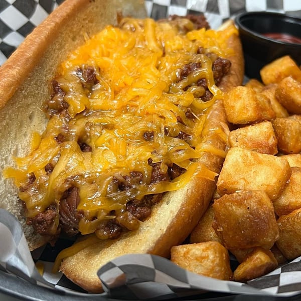 A chili cheese dog with melted cheddar and a side of crispy tater tots in a basket.
