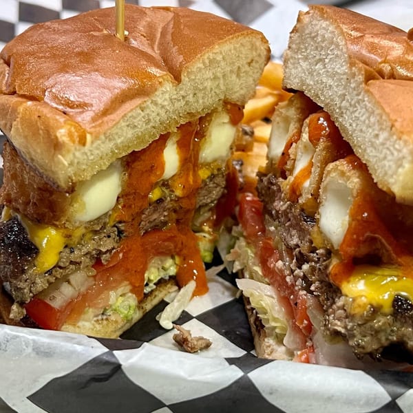 A large, messy burger from Life's Good Bar & Grill, cut in half, revealing melted cheese, sauce, and toppings.