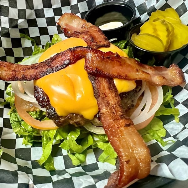 A bacon cheeseburger with lettuce, tomato, and onion, served with pickles and sauce.