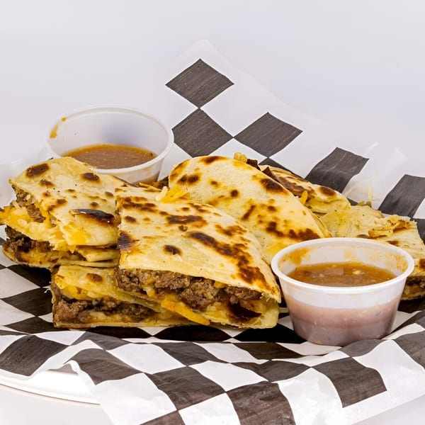 Beef and cheese quesadillas with two small cups of salsa, served on checkered paper.